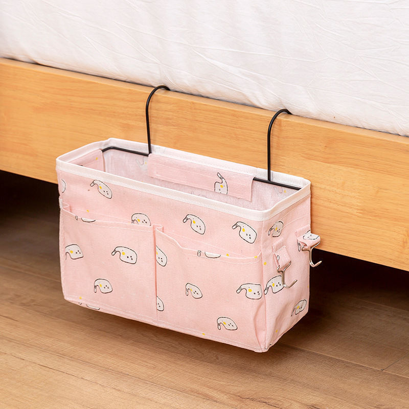 Pink canvas bedside storage bag with hooks, featuring multiple pockets for books, phone, and accessories. Available at Shopway.